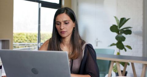 Indian professional woman working on laptop in modern minimalist coworking space focused