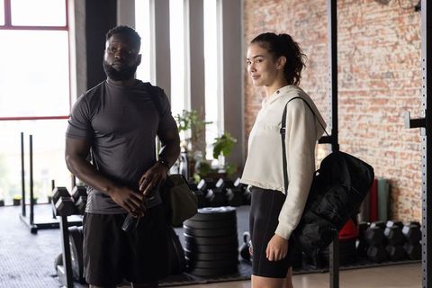 Diverse couple standing in industrial gym carrying duffel bags and water bottle