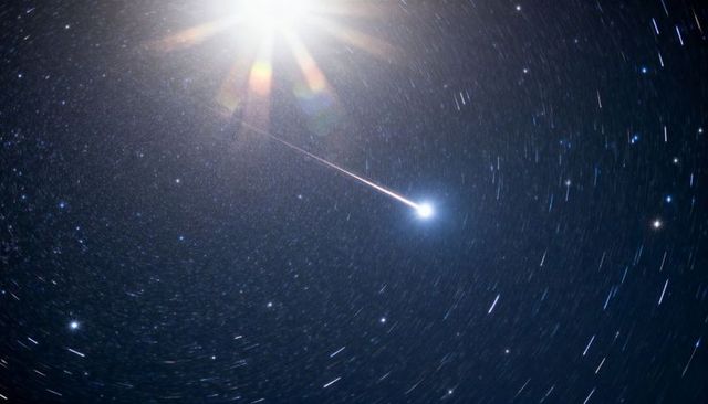 Bright bolide streaking through circular star trails with dramatic upper-left flare