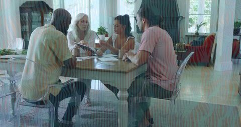 Diverse group reviewing paperwork and collaborating at sunlit home dining table with notebook