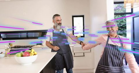 Mature couple holding hands dancing in bright modern kitchen with matching striped aprons