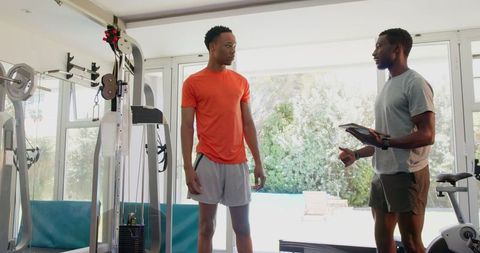 Man Working Out While Trainer Guides in Modern Gym