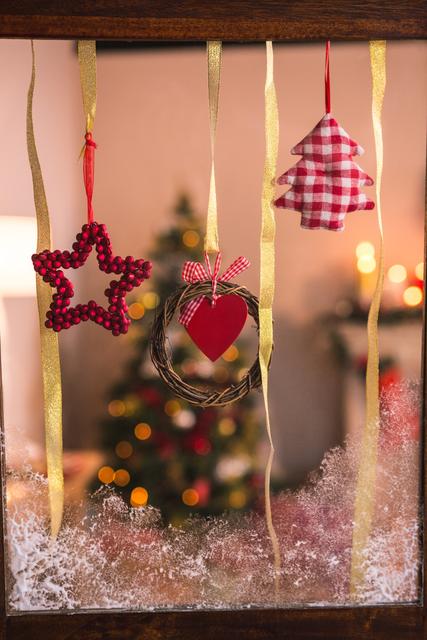 Christmas decorations including a grapevine wreath, a star, and a tree ornament hanging on a window with a Christmas tree in the background. Ideal for holiday greeting cards, festive home decor inspiration, or seasonal advertisements.