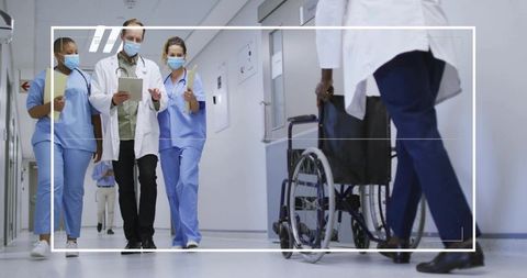 Multidisciplinary medical team walking hospital corridor with wheelchair and protective masks