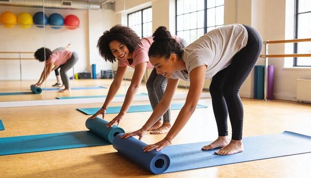Women rolling yoga mats together in bright studio preparing for barre and stretch class