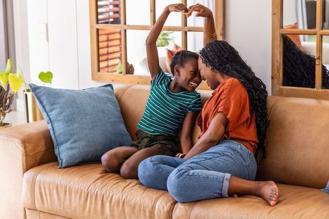 African american mother and daughter sharing heart gesture on cozy tan sofa