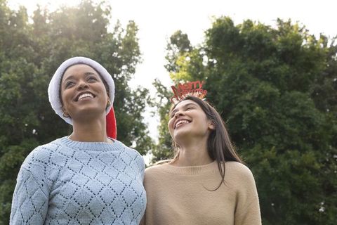 Diverse women smiling in park wearing santa hat and merry christmas headband, celebrating