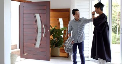 Father Congratulating Son in Graduation Attire at Home