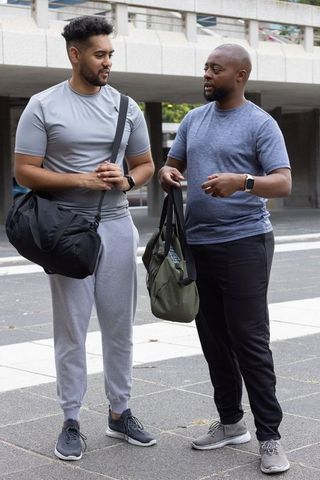 Two african american men talking after workout wearing smartwatches and carrying gym bags