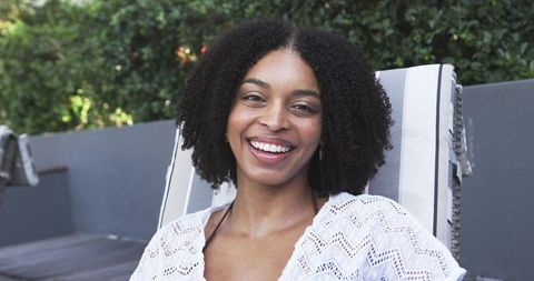 African american woman smiling and relaxing on striped lounge chair outdoors summer sunlight