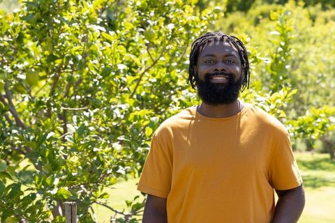 Smiling african american man in sunlit orchard wearing orange t-shirt, candid portrait