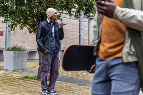 Skateboarding friends hanging out in urban plaza with vaping beanie and streetwear