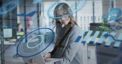 Businesswoman holding laptop smiling through glass with digital overlays in modern office