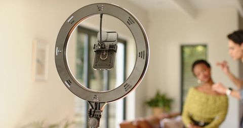 Led ring light with phone clamp capturing makeup tutorial in modern living room studio