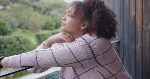African american woman gazing from balcony wearing knit sweater and smartwatch
