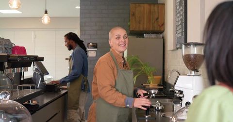 Smiling barista tamping espresso while colleague working behind modern urban cafe counter