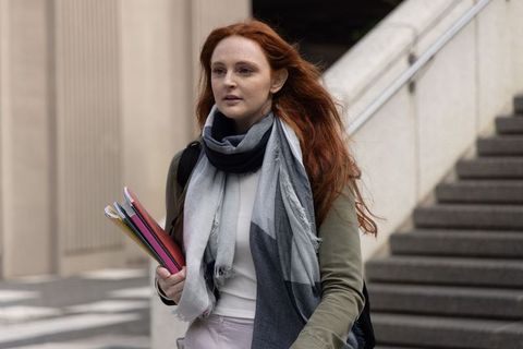 Red-haired student walking through city campus holding colorful notebooks and backpack