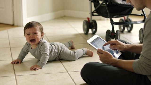 Crying infant on tiled floor with caregiver using tablet next to stroller at home
