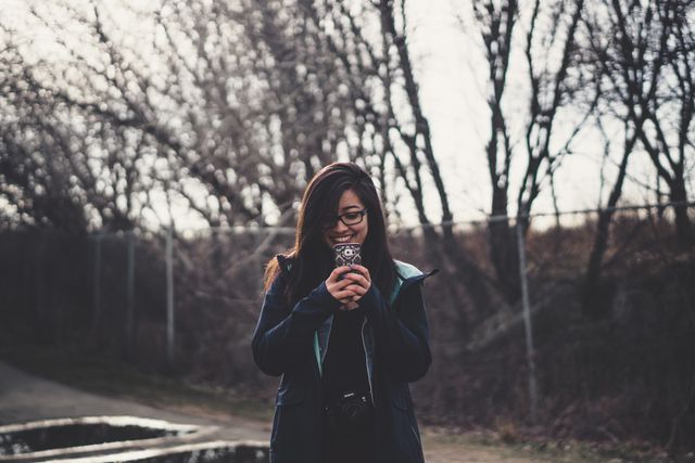 Woman enjoying outdoors in winter, taking photograph with phone. Useful for content on winter activities, outdoor lifestyle, photography hobbies, and happiness. Perfect for illustrating blog posts about enjoying nature, technology use in daily life, and seasonal outdoor fun.