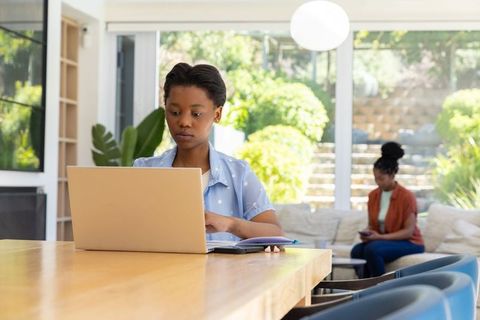 African woman and teenage female working remotely at home using laptop and smartphone