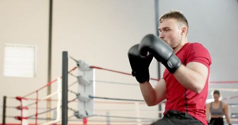 Male boxer training in ring wearing red shirt and black gloves holding guard