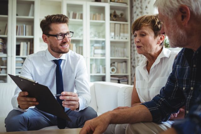 Senior couple consulting with a financial advisor in their living room. The advisor is holding a clipboard and discussing investment plans with the couple. This image can be used for financial services advertisements, retirement planning brochures, or articles about financial advice for seniors.
