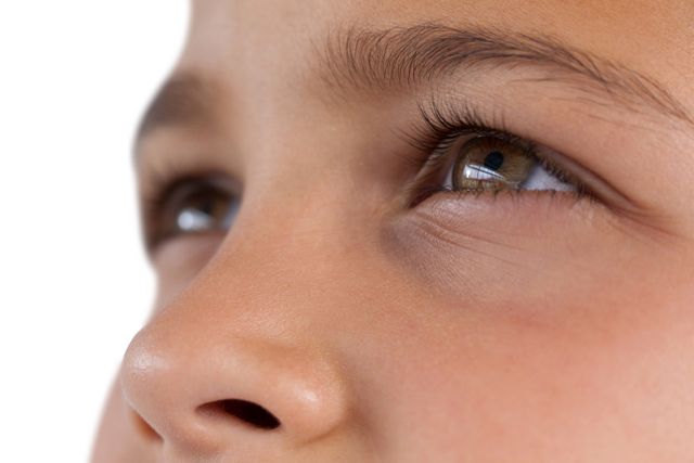 This close-up image captures a young boy with hazel eyes looking upwards, highlighting his eyelashes and smooth skin. The image conveys a sense of innocence and curiosity, making it ideal for use in educational materials, child-related advertisements, or articles about childhood and development.
