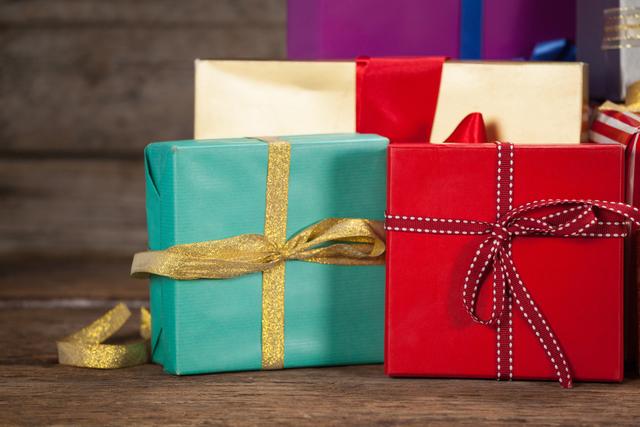 Colorful wrapped gift boxes with ribbons and bows on a wooden table. Ideal for holiday promotions, Christmas advertisements, festive greeting cards, and celebration-themed designs.