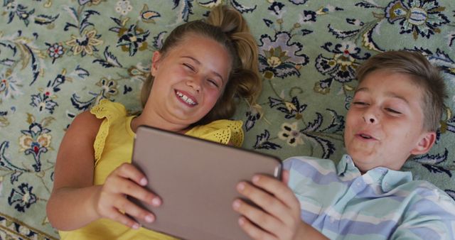 Happy caucasian brother and sister at home, lying on floor using tablet together and smiling - Download Free Stock Photos Pikwizard.com