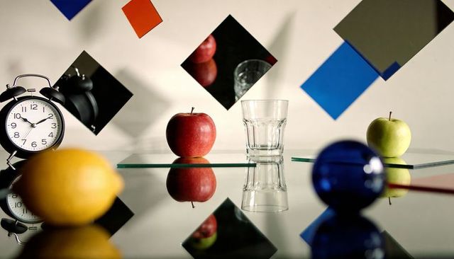 Glass tumbler on mirrored table with red and green apples, alarm clock and color blocks