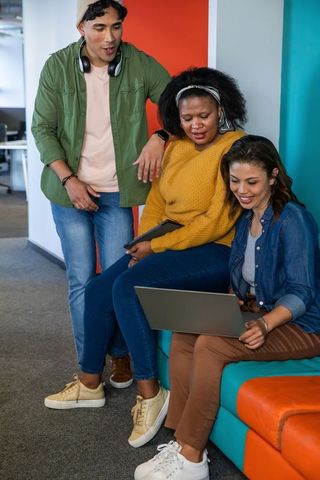 Diverse team collaborating on laptop in colorful office lounge for teamwork and creativity