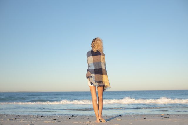 Rear view of woman wrapped in blanket standing on the beach