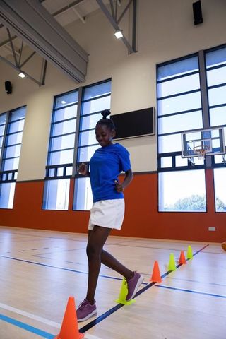 Young african american girl practicing agility cone drill in bright school gymnasium