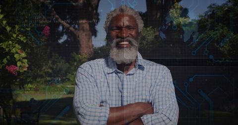 Smiling black senior man standing with arms crossed in garden wearing checked shirt
