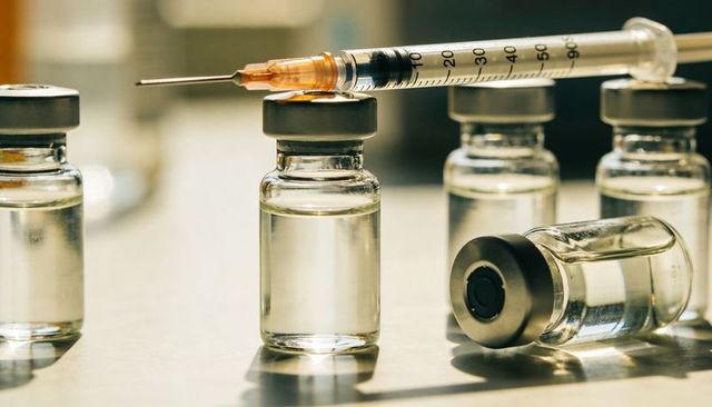 Vaccine vials and syringe resting on clinical bench with warm reflective lighting
