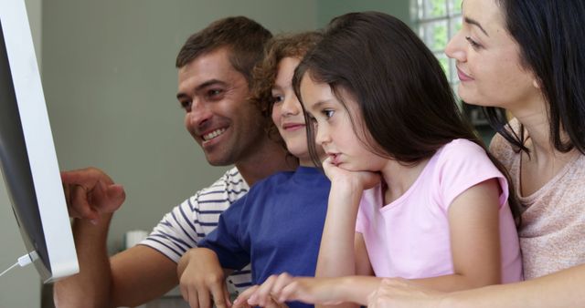 Parents and two young children enjoying quality time together while using a desktop computer at home. This image is ideal for illustrating family technology use, online learning, and digital bonding in marketing materials, educational content, and family-oriented advertisements.