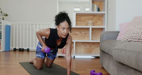African american woman performing kneeling dumbbell row during home workout session