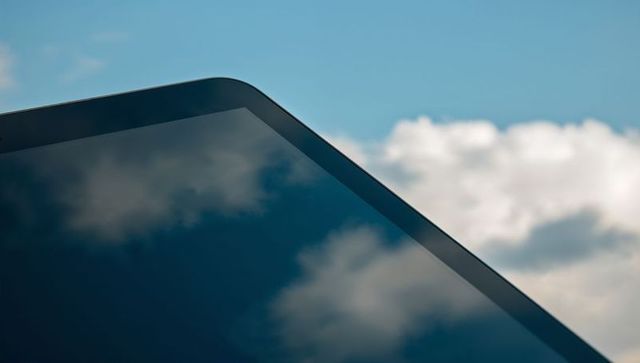 Glossy tablet reflecting clouds on blue sky, rounded bezel, sleek glass touchscreen