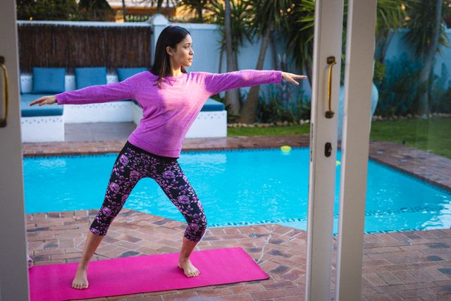 Woman practicing yoga on a mat by the poolside, ideal for promoting fitness, wellness, and healthy living. Perfect for use in lifestyle blogs, fitness websites, and wellness magazines.