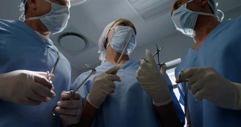 Surgical team performing operation in or wearing masks and gloves holding forceps and retractors