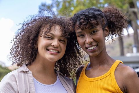 Sunlit diverse friends smiling and posing in park wearing vibrant yellow and purple tops