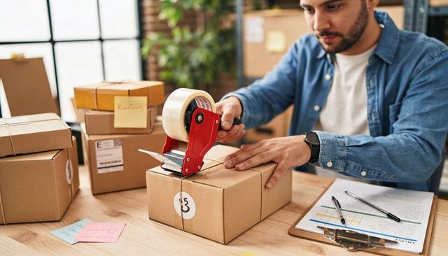 Small Business Owner Packing Parcels with Tape Dispenser in Bright Home Shipping Workspace