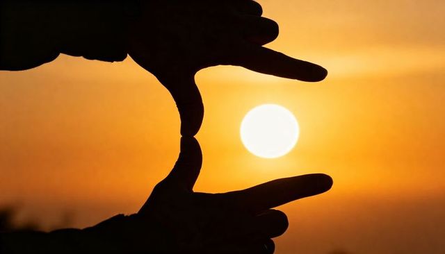 Hands framing sun during sunset silhouette creating golden horizon frame