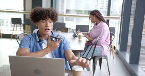Man Sends Voice Message While Working on Laptop in Cafe Setting