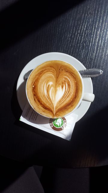 Top view of cappuccino with heart-shaped latte art on black table, perfect for coffee shop promotion, blog posts, social media, or coffee-related content. Creates warm, inviting atmosphere ideal for food and drink marketing.