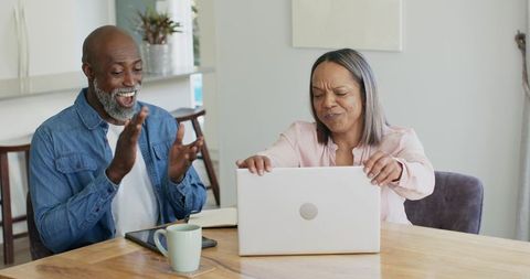 Mature couple celebrating virtual success as woman closing laptop while man clapping