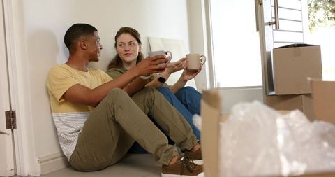 Couple unpacking boxes and sharing coffee on floor during move-in day, new home moment