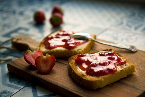 Spreading strawberry jam on toasted bread on rustic wooden cutting board