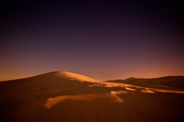 Night sky filled with stars forming radiant backdrop over sandy desert dunes. Ideal for nature-themed presentations, travel blogs, posters about solitude or adventure, environmental awareness campaigns, or concept art emphasizing tranquility and vastness.
