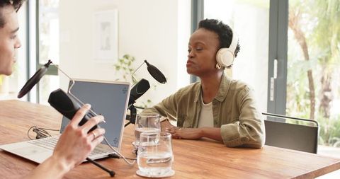 Diverse coworkers recording podcast interview with headphones and microphones